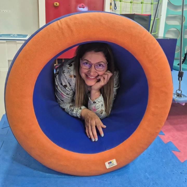 Eliana Arantes sorrindo dentro de um equipamento sensorial em formato de túnel, numa sala de Integração Sensorial